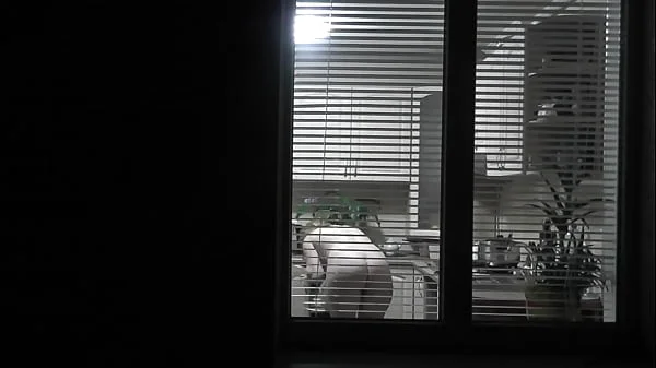 Peeping. Voyeur. Neighbor pervert voyeur in evening on street looks out window as naked sexy neighbor in kitchen prepares dinner for her husband. Naked in public. Naked at home. Family.  Outdoor